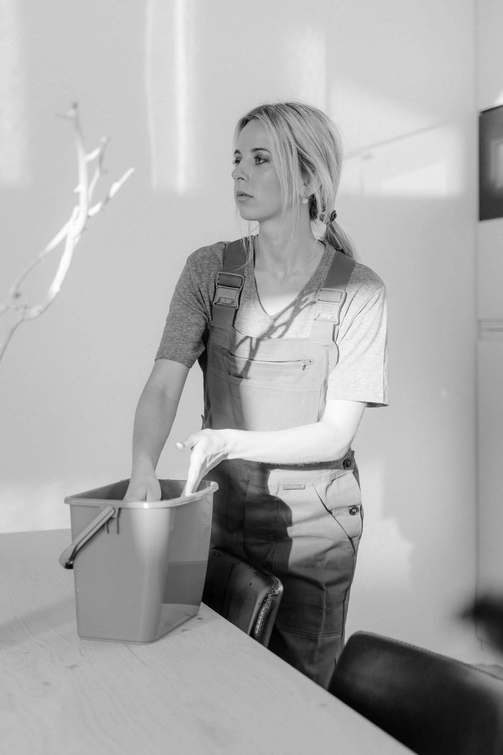 R&O Facilityservice – Eine Frau in einem roten Overall putzt in einem hellen, minimalistisch eingerichteten Raum und hält dabei einen blauen Eimer in der Hand.