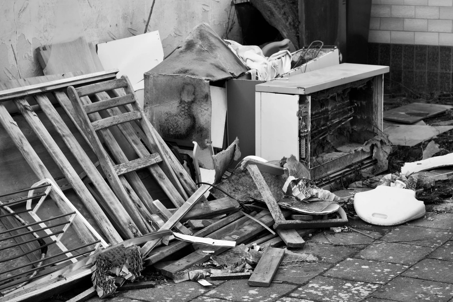R&O Facilityservice – Ein Haufen ausrangierter Möbel, Haushaltsgeräte und Schutt, der in Schwarz-Weiß an einer Wand aufgestapelt ist.
