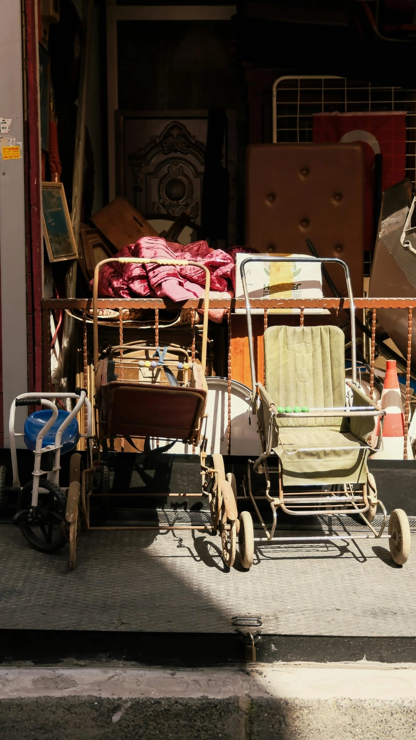 R&O Facilityservice – Vor einem überfüllten Antiquitätenladen, in dem alte Möbel und Bilderrahmen stehen, stehen zwei alte Kinderwagen.