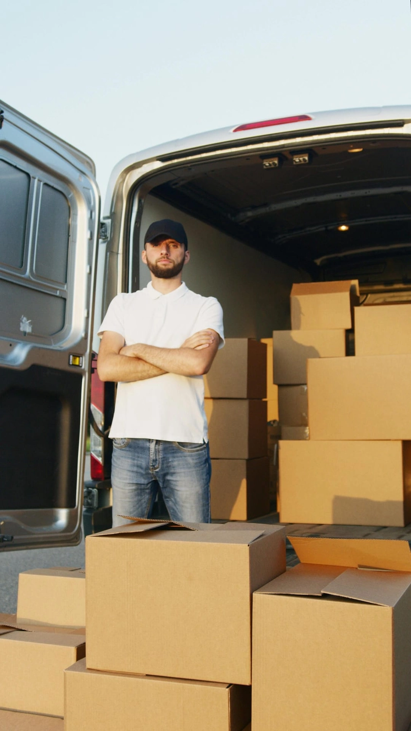 R&O Facilityservice – Ein Mann in einem weißen T-Shirt und einer Kappe steht mit verschränkten Armen vor einem mit Kartons beladenen Transporter.